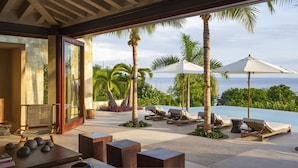 Ett modernt utomhusområde med loungekänsla, en pool, palmer och utsikt över havet.