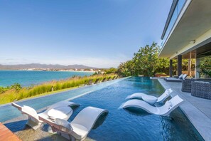 An infinity pool with white lounge chairs, a view of the sea, and a modern building structure. - Kupuri 32 In Kupuri Punta Mita (Punta de Mita)