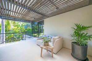 Un interior modern amb un balcó, un sofà, una taula petita amb una planta i una planta gran en test.