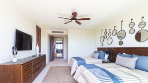 A bedroom with a TV, wooden dresser, two beds, a ceiling fan, and a hallway leading to another room. - Condo Ara in Punta Mita (Punta de Mita)