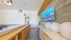 A modern kitchen with a wooden countertop, pendant lights, a large TV mounted on the wall, and a built-in oven. - Casa Brisa in Punta Mita (Punta de Mita)