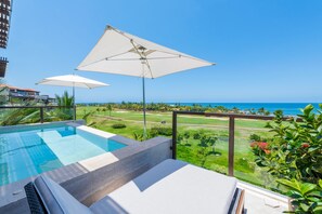 Ein Pool mit zwei Sonnenschirmen, Blick auf den Ozean und ein Golfplatz im Hintergrund.