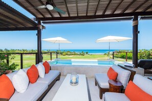 Ein überdachter Außenbereich mit Pool, weißen Kissen und zwei Sonnenschirmen.