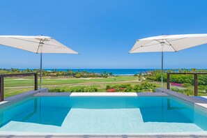 Ein Schwimmbecken mit zwei Sonnenschirmen, Blick auf den Ozean und ein Golfplatz im Hintergrund.