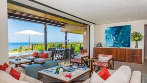 Ein modernes Wohnzimmer mit Meerblick, einem Essbereich und einem großen abstrakten Gemälde.