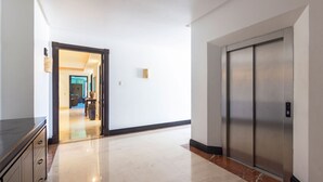 Un pasillo con piso de mármol, un ascensor y una puerta que da a otra habitación.