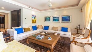 Una sala de estar moderna con sofá, mesa de centro y sillones, un comedor con mesa y sillas, y un pasillo que lleva a otra habitación.