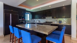 Una cocina moderna con armarios oscuros, una isla central con taburetes y electrodomésticos como refrigerador y estufa.