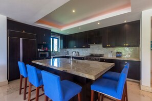 A modern kitchen with dark cabinetry, a central island with bar stools, a refrigerator, and a stove. - Condo Loto in Punta de Mita (Punta de Mita)