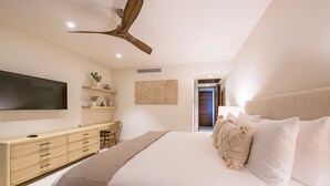 Een slaapkamer met een bed, een houten dressoir, een flatscreen televisie, een plafondventilator en een deur die naar een andere kamer leidt.