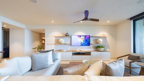 Een moderne woonkamer met een bank, fauteuils, een salontafel, een televisie en een plafondventilator.