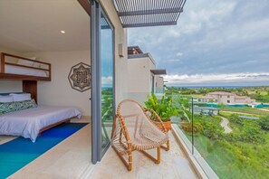 A balcony with a bed, a wicker chair, and a view of a green landscape. - Condo Las Olas in Punta Mita (Punta de Mita)