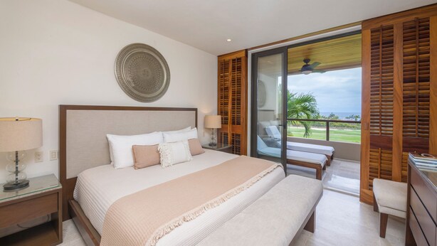 Ein Schlafzimmer mit einem großen Bett, einem Nachttisch, einem Fenster mit Holzläden und Blick ins Freie.