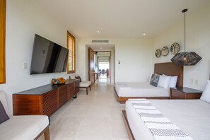 A modern hotel room with a large flat-screen TV, a wooden console, two beds, a seating area, and a hallway leading to a dining area. - Condo Aries in Punta Mita (Punta de Mita)