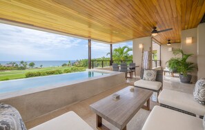 Ett takförsett utomhusområde med sittplatser, en pool, solstolar och utsikt över havet.