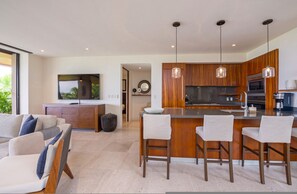 A modern kitchen with wooden cabinets, a central island with bar stools, pendant lighting, and a large window. - Condo Aries in Punta Mita (Punta de Mita)