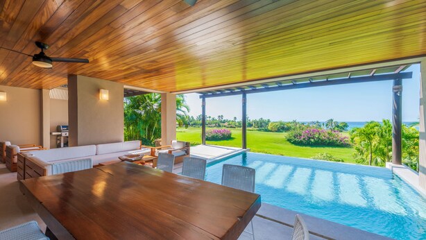 A modern outdoor pool area with a wooden ceiling, a dining table, and a view of a lush garden. - Condo Aquila in Punta Mita (Punta de Mita)