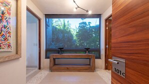 A hallway with a wooden bench, a large window with a view of trees, and a door with a sign. - Condo Aquila in Punta Mita (Punta de Mita)