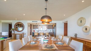 A dining area with a large wooden table, multiple chairs, and a hanging pendant light. - Condo Balboa in Punta Mita (Punta de Mita)