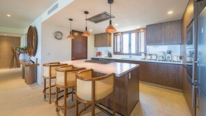 A modern kitchen with a central island, wooden bar stools, pendant lighting, and built-in appliances. - Condo Balboa in Punta Mita (Punta de Mita)