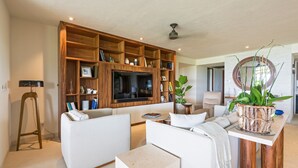 A modern living room with a large TV, wooden shelving, a sofa, a coffee table, and a potted plant. - Condo Balboa in Punta Mita (Punta de Mita)