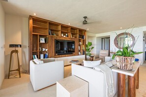 A modern living room with a large TV, wooden shelving, a sofa, a coffee table, and a potted plant. - Condo Balboa in Punta Mita (Punta de Mita)