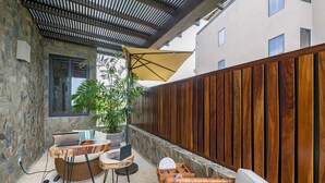 A patio area with a laptop on a wooden table, a wicker chair, a small table with a laptop, and a potted plant. - Condo Balboa in Punta Mita (Punta de Mita)