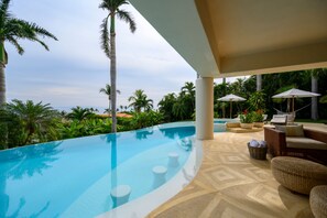 A swimming pool with a curved edge, surrounded by palm trees and lounge chairs. - Villa Alamanda in Punta Mita (Punta de Mita)