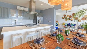 A modern kitchen with white cabinetry, a central island, and a dining area with a wooden table set for four. - Condo Terramar in Punta Mita (Punta de Mita)