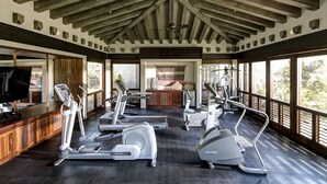 Een sportschool met trainingsapparatuur, houten balken, grote ramen en een televisiescherm.
