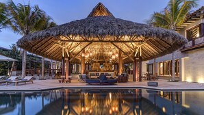 Een resort met een zwembad, een loungeruimte met rieten dak en palmbomen.
