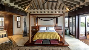 Ruime slaapkamer met een groot bed, houten balken, een plafondventilator en uitzicht op de omgeving.
