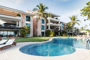 A resort with a swimming pool, palm trees, and a multi-story building with balconies. - Condo Clavel in Punta Mita (Punta de Mita)
