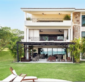Une maison à deux étages dotée d’un patio couvert, de meubles d’extérieur et offrant une vue sur l’océan.