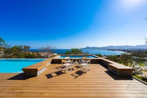 A wooden deck with a pool, chairs, and a table overlooking a body of water and mountains. - Villa Vera in Punta Mita (Punta de Mita)