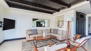 A modern living room with a sofa, coffee table, and chairs, a flat-screen TV, and a large mirror. - Condo Aralia in Punta Mita (Punta de Mita)