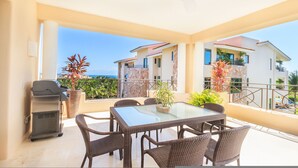 A balcony with a glass table, wicker chairs, a grill, and potted plants. - Condo Aralia in Punta Mita (Punta de Mita)
