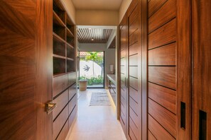 A hallway with wooden doors, a tiled floor, and a view of an outdoor area with plants. - Villa Aurora in Punta Mita (Punta de Mita)