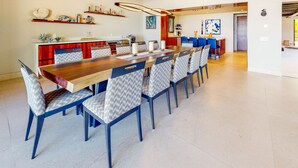 Een moderne eetruimte met een lange houten tafel, blauwe stoelen en een keuken op de achtergrond.