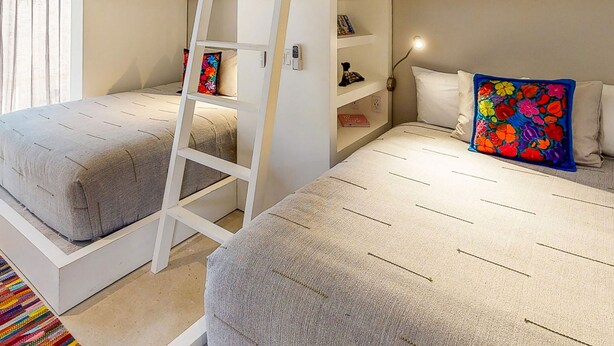 Een kamer met twee bedden, een ladder, een plank met boeken en een kleurrijk kleed.