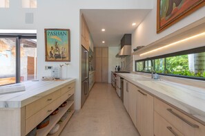 Une cuisine moderne avec des meubles en bois, un plan de travail en marbre et une grande fenêtre donnant sur un paysage verdoyant.