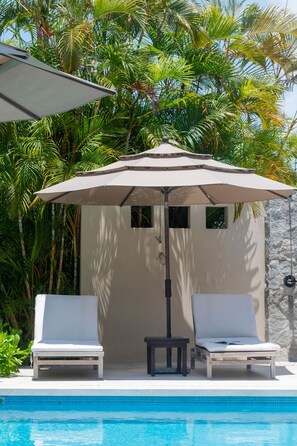 Un espace aménagé au bord de la piscine, comprenant deux chaises longues, une table et un parasol.