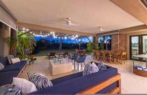 En udendørs terrasse med sofa, stole, spisebord og ventilator.