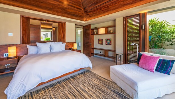 Une chambre avec un grand lit, un plus petit lit, un plafond en bois, une table de chevet et une commode, ainsi qu’une fenêtre donnant sur un paysage verdoyant.