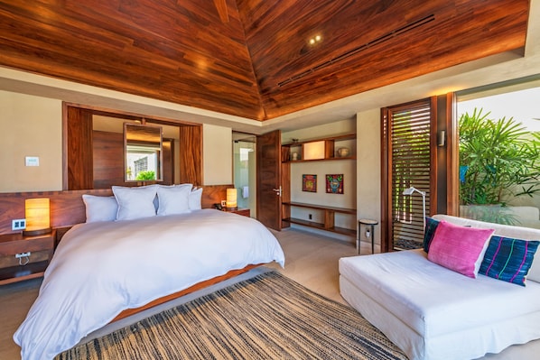 A bedroom with a large bed, a smaller bed, a wooden ceiling, a nightstand, a bedside table, and a window with a view of greenery. - Estate Taurus in Kupuri Oceanfront Private Pool Design (Punta de Mita)