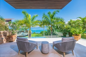 A balcony with two grey chairs, a round table, and a view of the ocean. - Estate Taurus in Kupuri Oceanfront Private Pool Design (Punta de Mita)