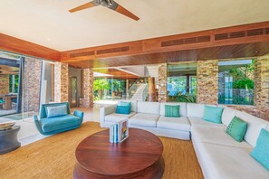A spacious living area with a large white sectional sofa, a round wooden coffee table, and a ceiling fan. - Estate Taurus in Kupuri Oceanfront Private Pool Design (Punta de Mita)
