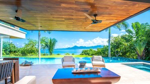 Un espace de détente extérieur moderne, doté d’une piscine, d’un plafond en bois et offrant une vue sur l’océan.