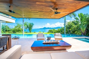 A modern outdoor lounge area with a pool, wooden ceiling, and a view of the ocean. - Estate Taurus in Kupuri Oceanfront Private Pool Design (Punta de Mita)