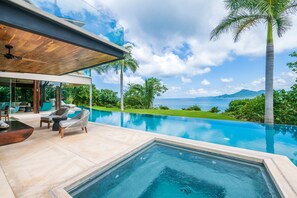 Ein moderner Poolbereich mit Blick aufs Meer, Gartenmöbel und einem klaren Himmel.